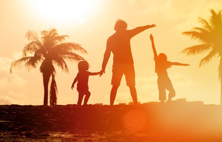 father with son and daughter silhouettes play at sunset skyの写真素材