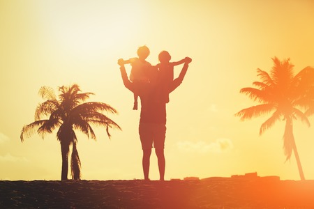 silhouette of father wither two kids play at sunset tropical beachの写真素材