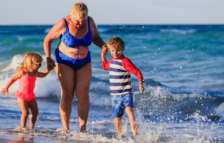 Happy grandmother with kids- little boy and girl- play at tropical beach