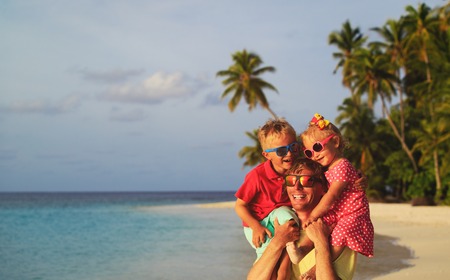happy father with two kids on shoulders at sky on beachの写真素材