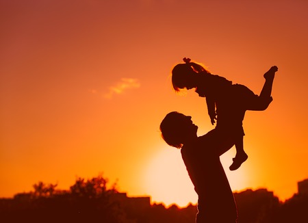 Father and little daughter silhouettes play at sunset skyの写真素材