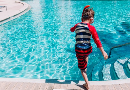 Little boy jumping into swimming pool, family vacation