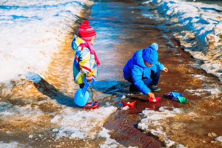 little boy and girl plaing with paper boats in spring puddleの写真素材