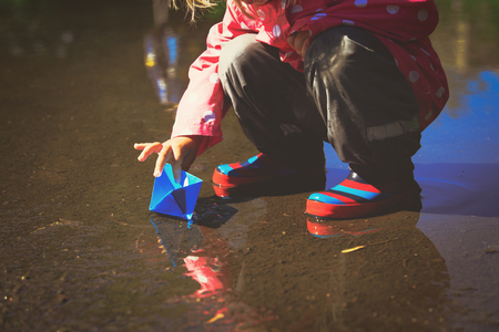 little girl playing with paper boats in puddleの写真素材