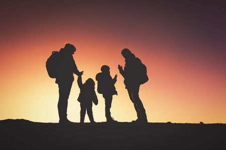Silhouettes of happy family with two kids hiking at sunsetの写真素材