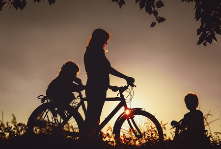 mother with son and daughter riding bike at sunsetの写真素材