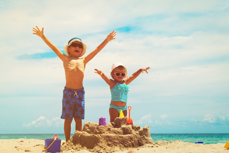 little boy and toddler girl play with sand on beachの写真素材