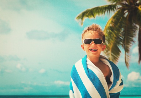 happy little boy wrapped in towel at beachの写真素材