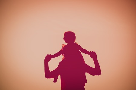 father and little daughter on shoulders play at sunset skyの写真素材