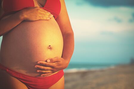 Happy pregnant woman at sunset beachの写真素材