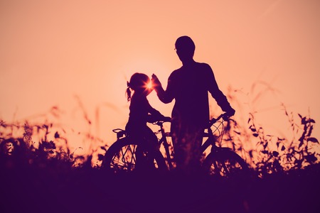father and daughter riding bike at sunsetの写真素材