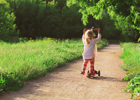 little girl riding scooter in summerの写真素材
