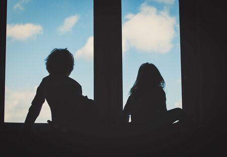 little girl and boy looking through the windowの写真素材