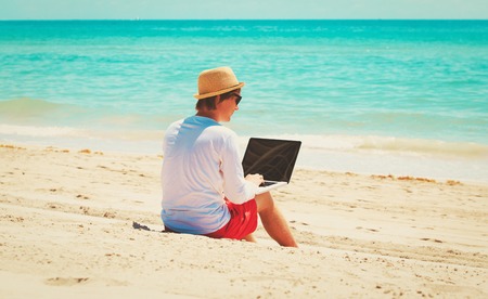 man working on laptop at tropical beachの写真素材