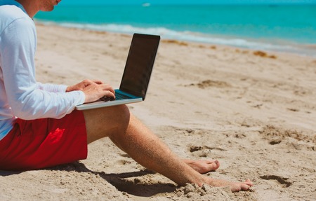 man working on laptop at tropical beachの写真素材