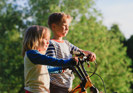 little girl and boy riding bikes in natureの写真素材