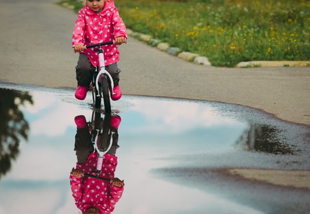 little girl riding bike in water after rain, kids outdoorの写真素材