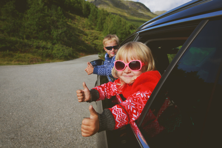 happy little boy and girl travel by car in mountainsの写真素材