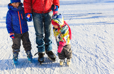father teaching two kids to skate in winterの写真素材