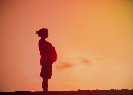 Silhouette of happy pregnant woman at sunsetの写真素材