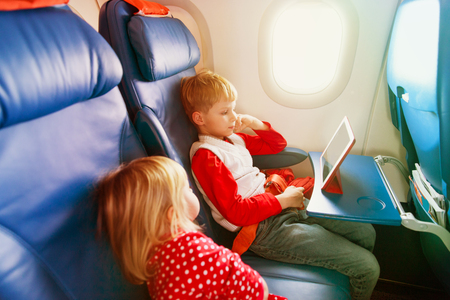 little girl and boy watching touch pad travel by planeの写真素材