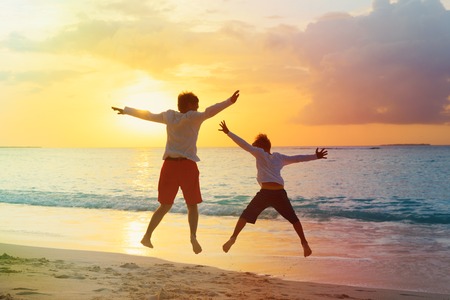 father and son have fun jump at sunset beachの写真素材
