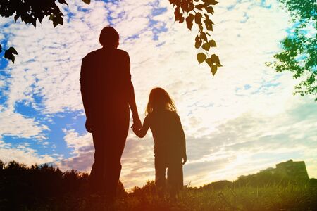silhouette of father and daughter holding hands at sunsetの写真素材