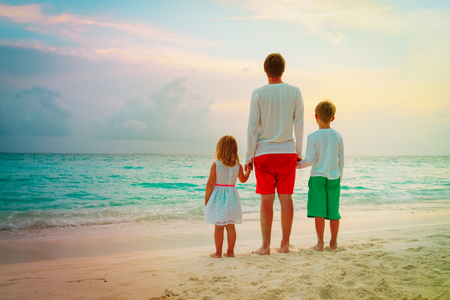 father with son and daughter holding hands at sunset beachの写真素材