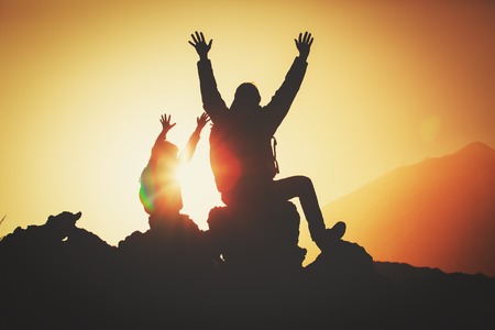 Silhouettes of father and son hiking in mountains at sunsetの写真素材