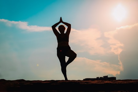 silhouettes of senior woman doing yoga at sunset skyの写真素材