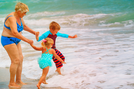 Happy grandmother with kids- little boy and girl- play on beachの写真素材