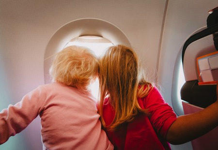 kids plane travel- little girls looking in window on flightの写真素材