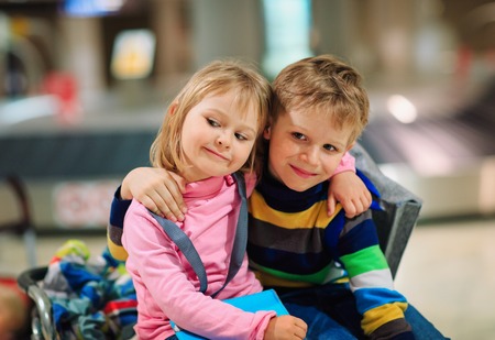 little boy and girl wait in airport, sit on luggage, family travel