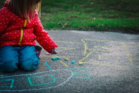 little girl drawing with chalks on playground