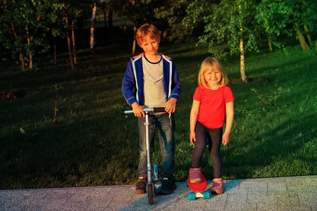 happy kids-little boy with scooter and girl on skateboard ride outside