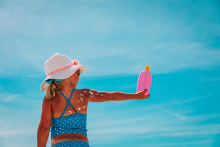 sun protection at beach- little girl applying sunblock cream on shoulderの写真素材