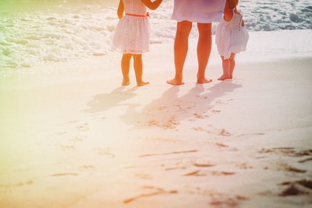 Mother with two daughters walk on sand beach