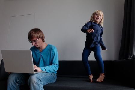 father try to work from home while little daughter jump dance make noiseの写真素材