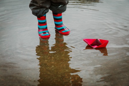child playing with paper boats in water puddle