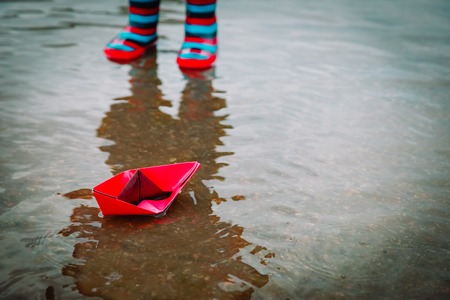 child playing with paper boats in water puddle