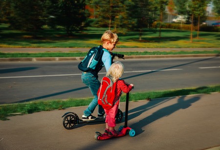 little boy and baby girl riding scooters in the cityの写真素材