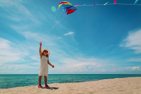 Little girl flying a kite at sky on beachの写真素材