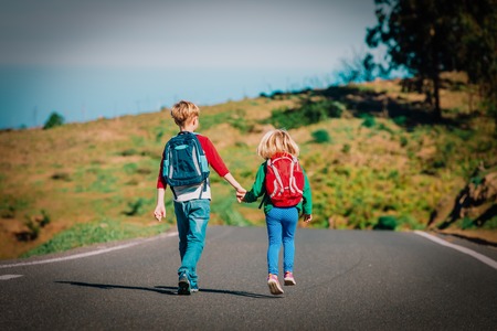 kids go to school - brother and sister with backpacks walking on road