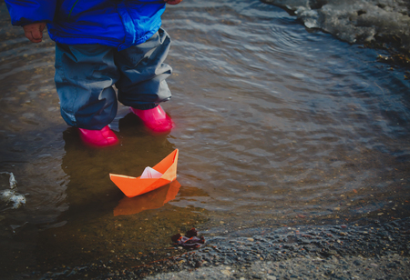 little girl playing with paper boats in water puddleの写真素材
