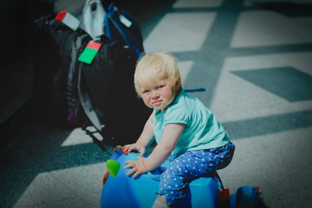 cute little baby with backpack and suitcase wait in airport, family travelの写真素材