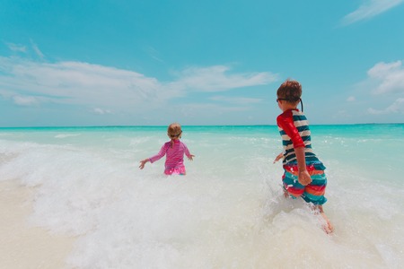 little girl and boy run play with waves on beachの写真素材