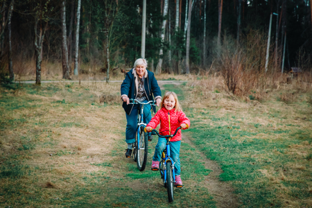 senior grandmother with granddaughter riding bikes in natureの写真素材