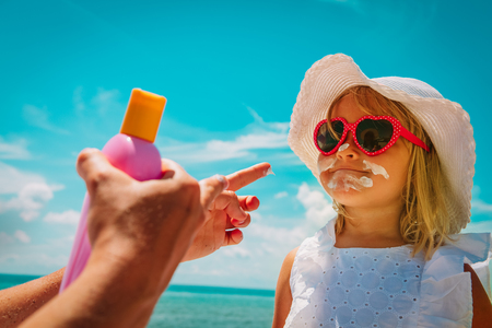 sun protection - mom put suncream on little girl face at beachの写真素材