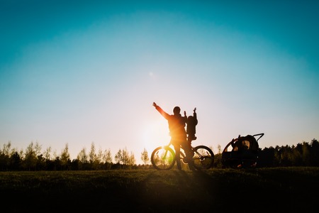happy father and little daughters riding bike at sunsetの写真素材