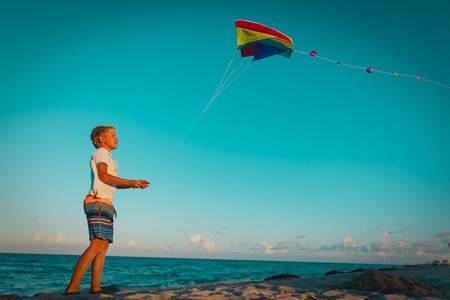Young boy flying a kite on tropical beach at sunsetの写真素材